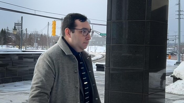 Un homme avec un manteau gris et cravate rayée à l'entrée du palais de justice de  Moncton.