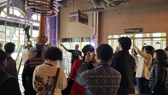 Des personnes sont amassées en cercle autour du propriétaire de la distillerie, Jacques Tremblay, qui explique le fonctionnement de la distillation. 