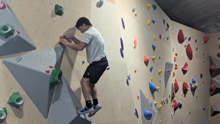 Un personne grimpe sur un mur d'escalade dans un bâtiment.