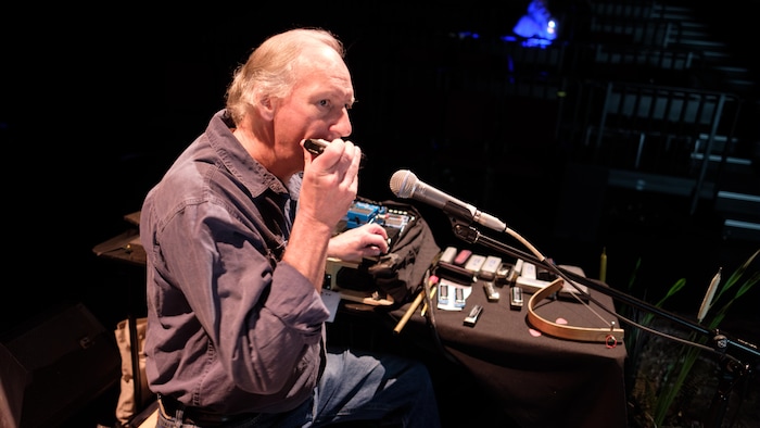 Gérald Laroche joue de l'harmonica devant un microphone.