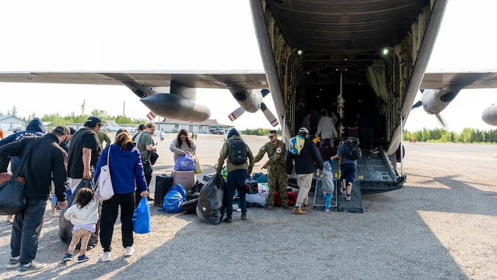 Des personnes avec des sacs entre dans un avion militaire.