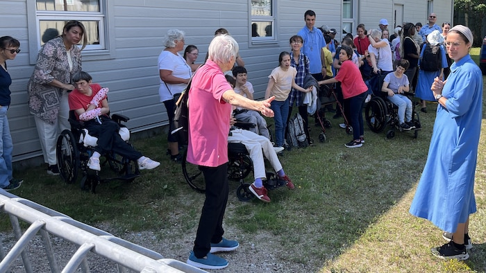 Plusieurs personnes font la file à côté d'un bâtiment. Certaines sont en fauteuils roulants.