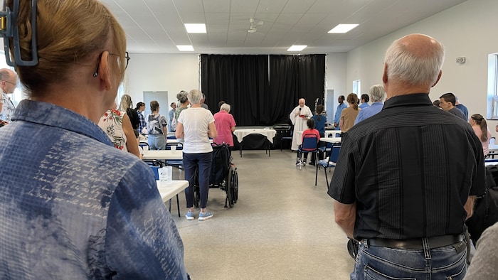 Des gens écoutent un prêtre dans une salle.