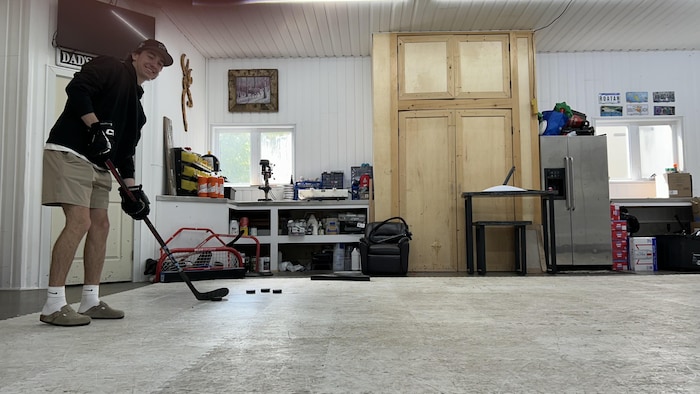 Un jeune homme qui prend un lancer de hockey sur des tuiles synthétiques dans un garage.