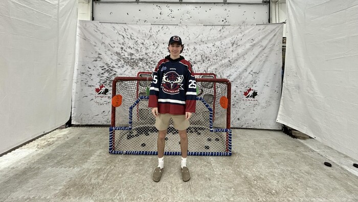 Un jeune garçon devant son filet de hockey dans un garage. On voit plusieurs marques de hockey sur un mur blanc en arrière-plan.
