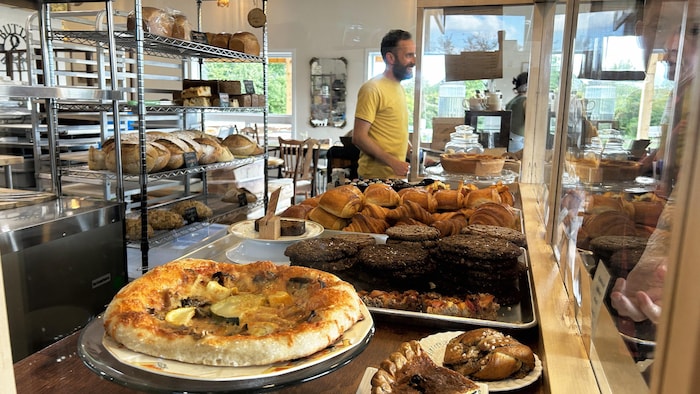 Des pâtisseries et des plats dans une boulangerie. Un homme sert un client en arrière-plan.