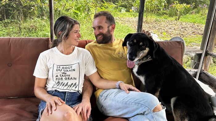 Une femme, un homme et un chien assis sur un fauteuil. La femme et l'homme se regardent en souriant.