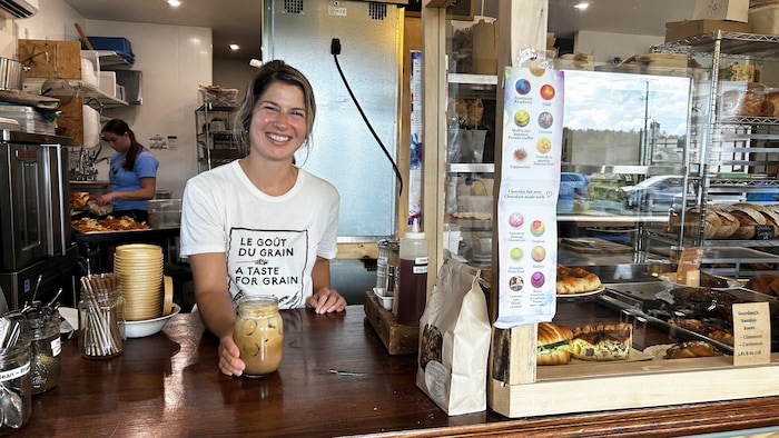 Une femme souriante qui sert un breuvage sur un comptoir d'un café.