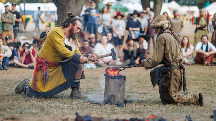 Deux personnes costumées qui façonnent une pièce de métal à l'aide d'outils de forgeron lors d'un festival médiéval.