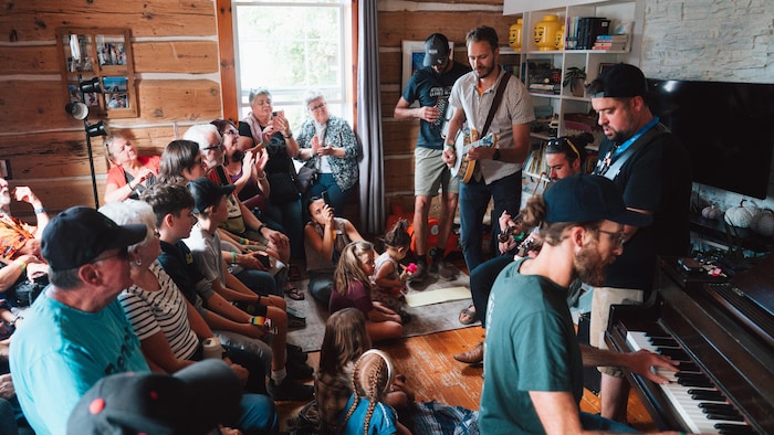 Des musiciens qui performent devant un public dans le salon d'une maison.