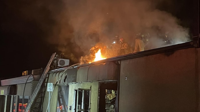 Des pompiers tentent d'éteindre des flammes apparentes sur le toit d'un bâtiment commercial.