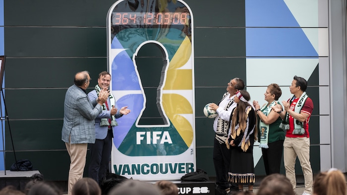 Des spectateurs observent un panneau affichant le décalque du trophée de la Coupe du Monde de soccer, surplombé d'un décompte à Vancouver, en juin 2025.