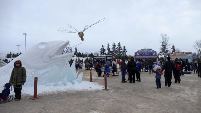 Des visiteurs marchent autour d'une statue de glace en forme de poisson et des kiosques de nourriture.