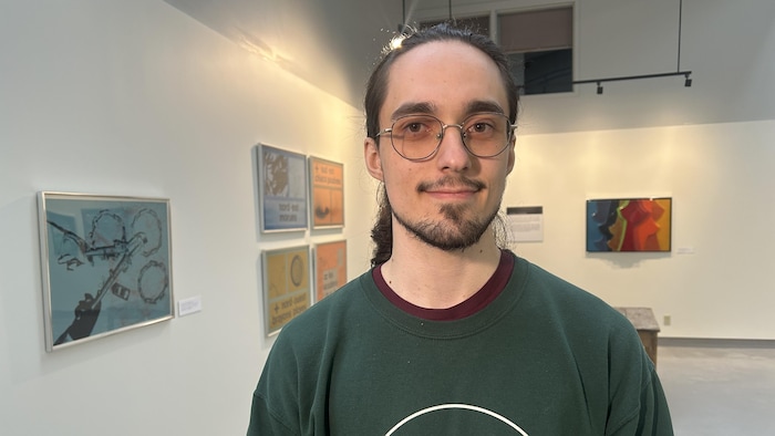 Un jeune homme portant des lunettes devant des œuvres d'arts. 