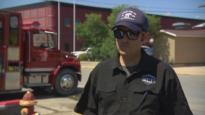 A firefighter in sunglasses stood in front of a truck. gradual return flin flon despite