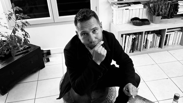 Un homme qui pose assit à une table de salon.