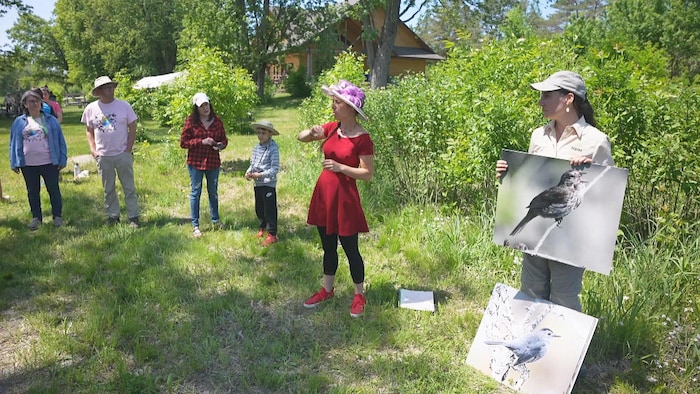 Des adultes et un enfant se tiennent debout dans un parc national. À l'avant-plan, une femme donne des explications et une autre tient deux agrandissements de photos d'oiseaux.