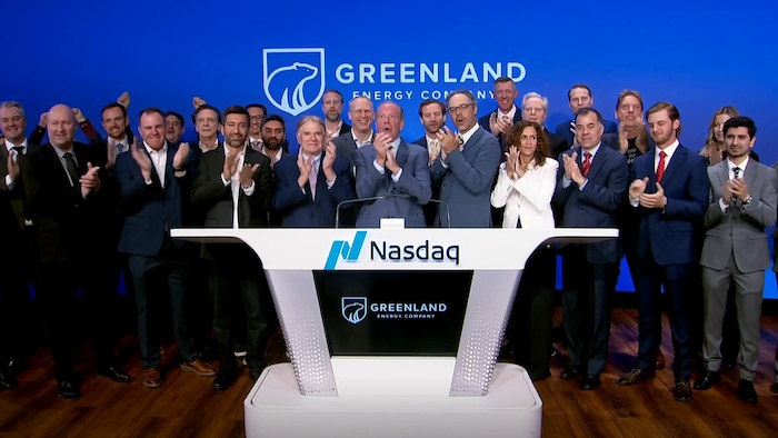 Des personnes applaudissent devant un bureau marqué NASDAQ et devant un écran frappé du logo de Greenland Energy.