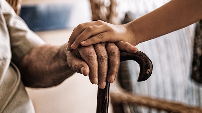 La main d'une jeune personne sur la main d'une personne âgée appuyée sur une canne.