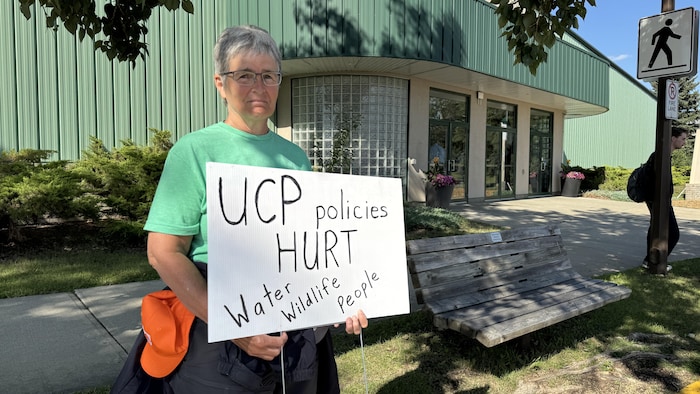 Heather Plaizier tient une pancarte sur laquelle est inscrite en anglais « les politiques du PCU nuisent à l'eau, la faune et les gens ».