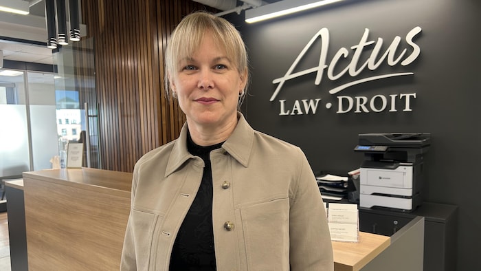 Une femme sourit devant un bureau. 