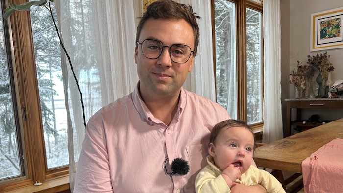 Martin Rioux sourit à la caméra en tenant son bébé. 