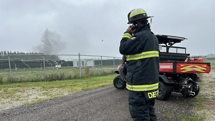Un pompier devant un incendie derrière une clôture.