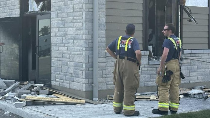 Deux pompiers devant un immeuble endommagé. 