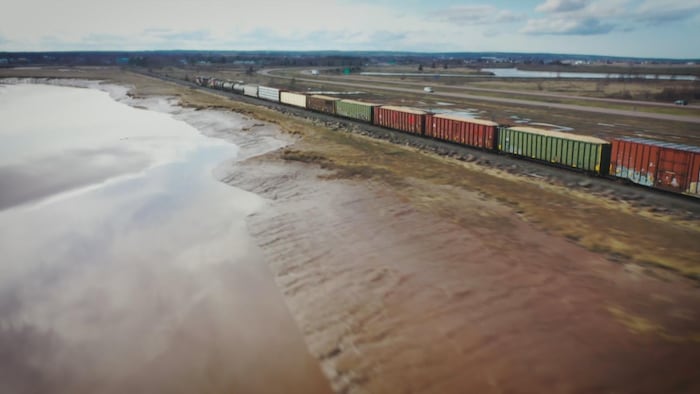 Un train de plusieurs wagons roule sur un chemin de fer le long de l'eau.