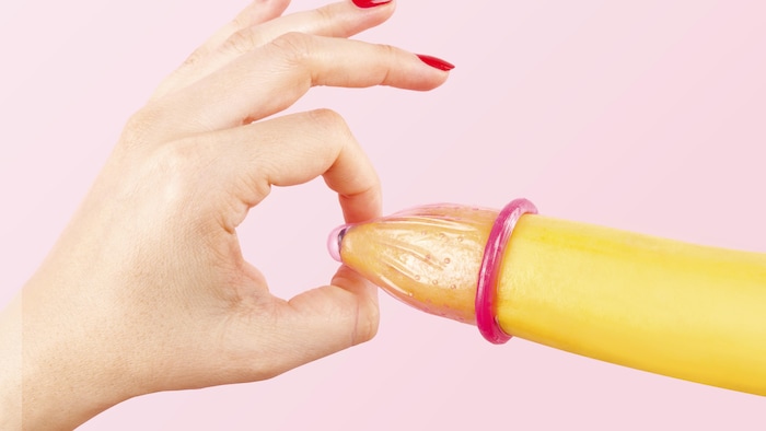 La mano de una mujer con las uñas rojas coloca un preservativo en un plátano. 