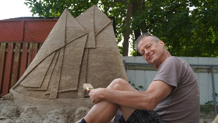 James W. Cook devant un bateau sculpté dans le sable.