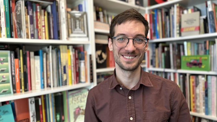 Un homme souriant qui pose devant des bibliothèques remplies de livres.