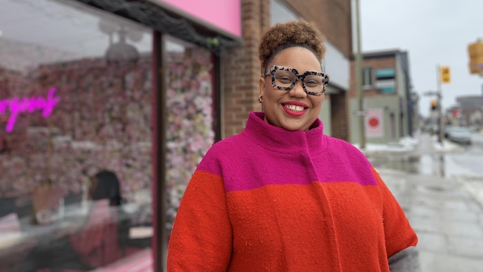 Une femme souriante qui pose devant une boutique sur le bord d'une rue.
