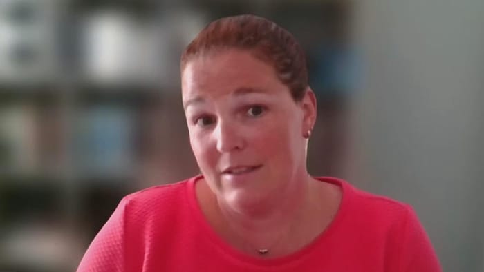Une femme blanche avec un Tshirt rose fuchsia parle à la caméra en Zoom.