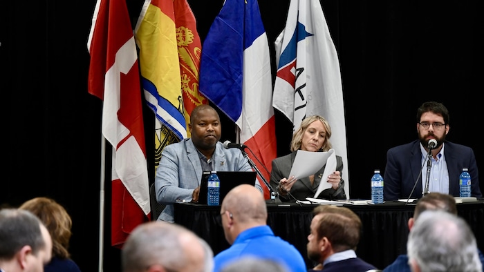 Kassim Doumbia et deux autres membres de l'AFMNB sont assis à une table munie de micros devant une foule à Moncton.