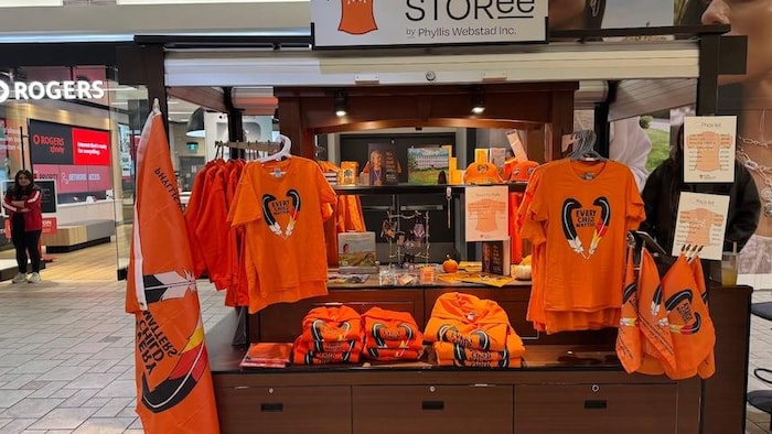 Des chandails, des drapeaux et d'autres produits oranges sont exposés à un kiosque d'un centre commercial.