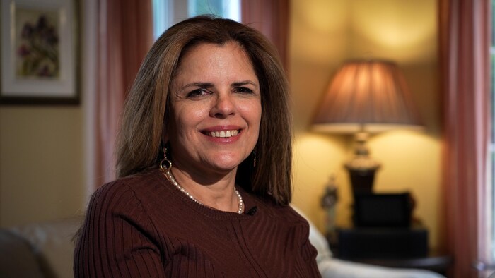 Une femme souriante qui pose assise sur une chaise dans un salon.