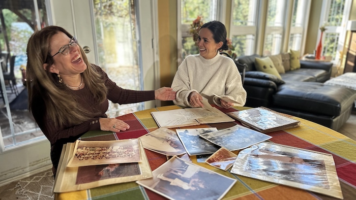 Deux femmes qui rient. Elles sont assises &agrave; une table sur laquelle se trouvent plusieurs photographies.