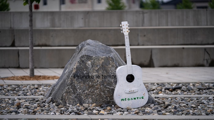 Une roche sur laquelle il est écrit "prendre le temps". À côté, une guitare est peinte en blanc., 