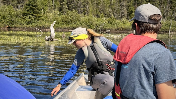 Des personnes dans une chaloupe naviguent sur un lac. Quelqu'un tend sa main vers l'eau.