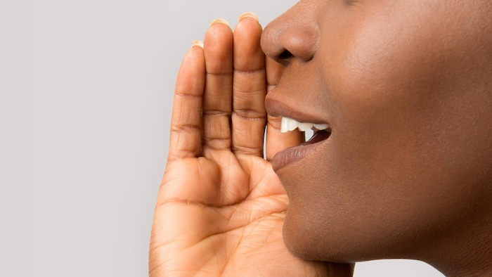 Gros plan du profil d'un visage d'une femme. Elle est en train de parler avec sa main placée près de sa bouche.