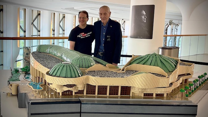 Deux hommes qui posent derrière une grande représentation du Musée canadien de l’histoire en Lego.