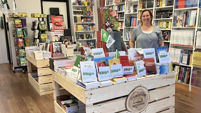 Une femme qui pose derrière une table remplie de livres dans une librairie.