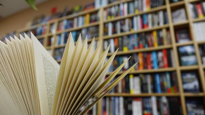 En avant-plan, un livre ouvert devant une bibliothèque bien remplie.