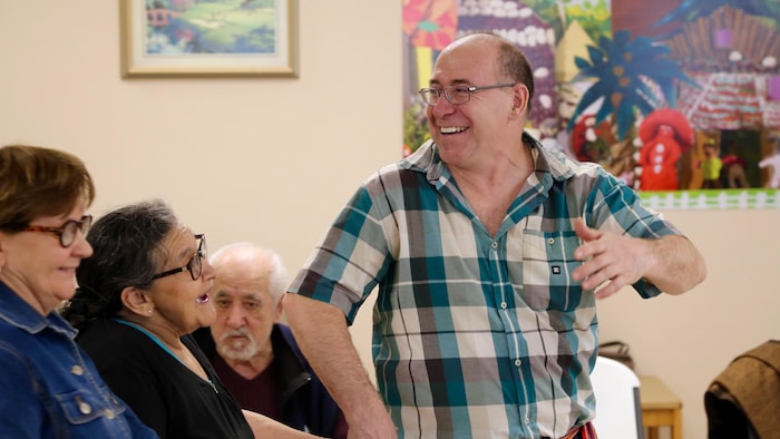 Un homme souriant debout. Il est entouré de personnes positive âgées assises.