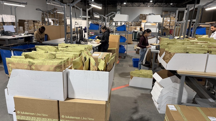 Des personnes travaillent dans un entrepôt. On voit des enveloppes de vêtement dans des cartons.