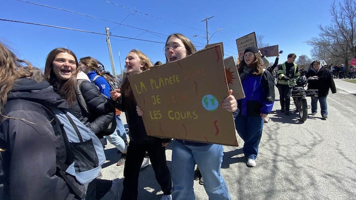 Des manifestants marchent. Une femme tient une affiche sur laquelle il est écrit «La planète sèche, je sèche les cours». 