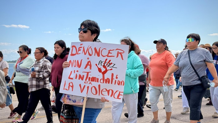 Des gens marchent dans la rue, une personne tient une pancarte contre l'intimidation et la violence.