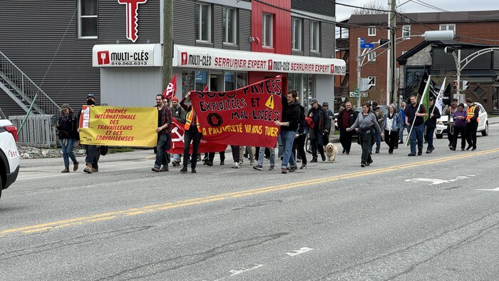 Une trentaine de personnes marchent. Certaines d'entre elles tiennent notamment une affiche qui porte la mention « Sous-payées, exploitées et mal logées – La pauvreté va nous tuer ».