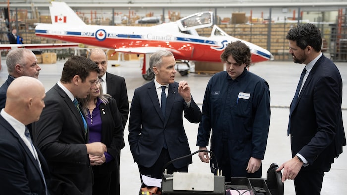 Des hommes discutent dans une usine avec un avion en arrière-plan.